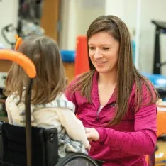 A woman working with a child in a wheelchair to overcome challenges.